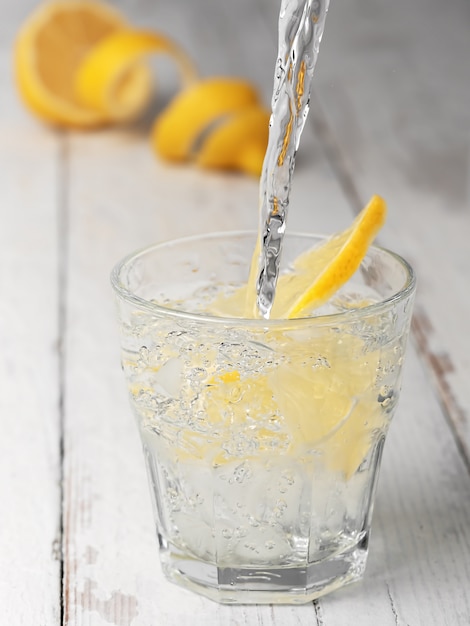 Verter la limonada en un vaso con hielo, fondo blanco de madera vintage.