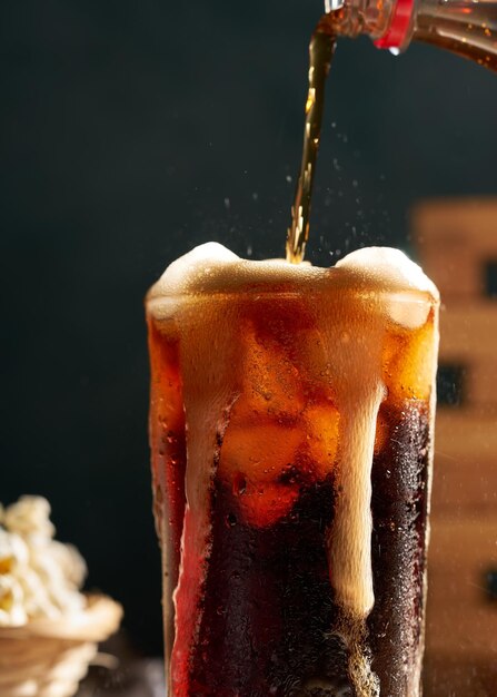 Foto verter refresco de cola en un vaso sobre una mesa de madera con palomitas de maíz