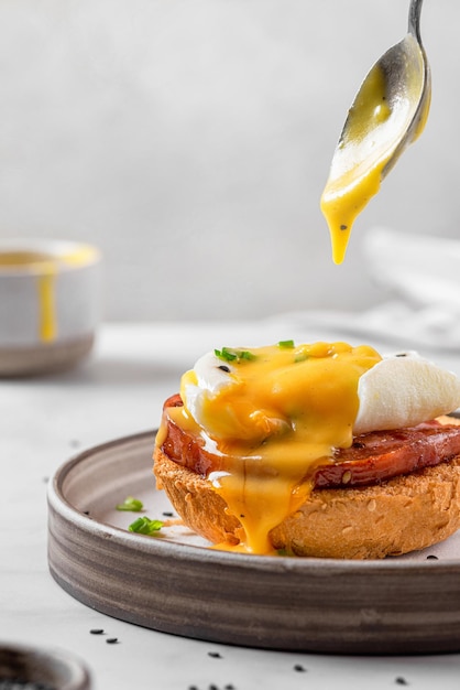 Verter salsa holandesa en huevo benedictino con cebolla de jamón de huevo escalfado en rebanadas tostadas para un sabroso desayuno brunch inglés de orientación vertical