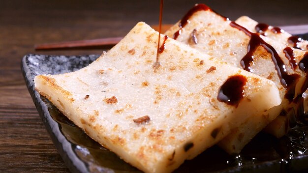 Verter salsa de soja negra en un delicioso pastel de nabo listo para comer, pastel de rábano plato local tradicional chino en el restaurante, de cerca, copie el espacio.