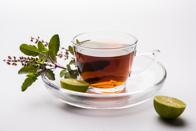 Verter el té de albahaca santa o tulsi en un vaso de vidrio transparente con platillo sobre fondo blanco o negro. Medicina ayurvédica popular de la India