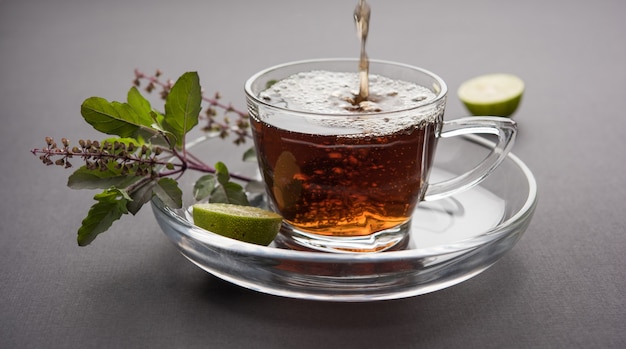 Verter el té de albahaca santa o tulsi en un vaso de vidrio transparente con platillo sobre fondo blanco o negro. Medicina ayurvédica popular de la India