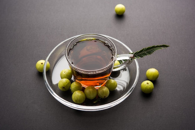 Verter el té amla o Avla Chai en un vaso de vidrio transparente con platillo sobre fondo blanco o negro. Medicina ayurvédica popular de la India