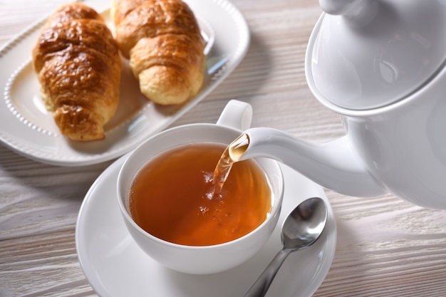 Verter té caliente en una taza sobre fondo blanco de mesa