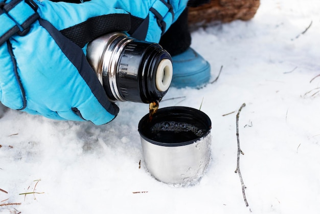 Verter té caliente en una taza de termo. Concepto de turismo, deportes y viajes de invierno.