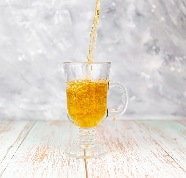 Verter té negro en un vaso sobre la mesa de madera y pared gris