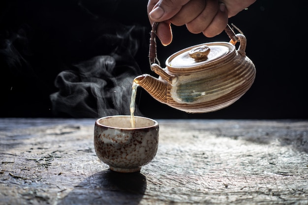 Verter té en tetera y taza de cerámica con vapor sobre fondo de madera