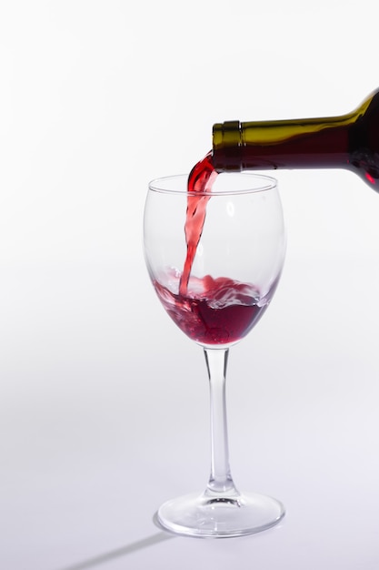 Verter el vino tinto de botella en vaso grande sobre fondo blanco.