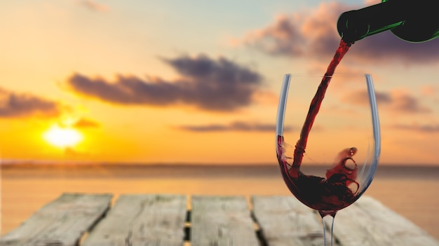 Verter el vino tinto en un vaso sobre fondo natural puesta de sol