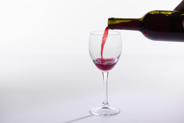 Verter el vino tinto en vidrio de botella sobre fondo blanco con espacio de copia