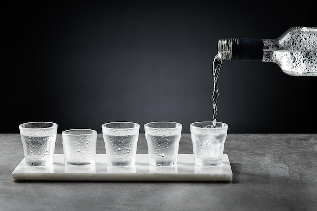 Verter vodka frío en vaso de chupito aislado sobre fondo oscuro. Enfoque selectivo.