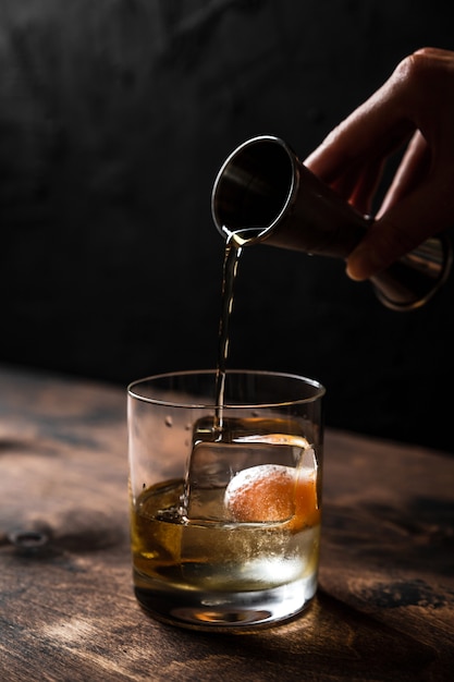 Verter whisky de un aparejo en un vaso bajo con un gran cubo de hielo