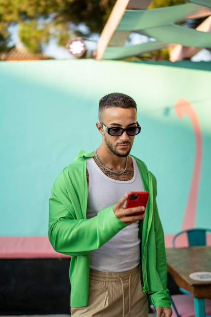 Foto vertical de un atractivo joven español barbudo con ropa elegante mirando su smartphone