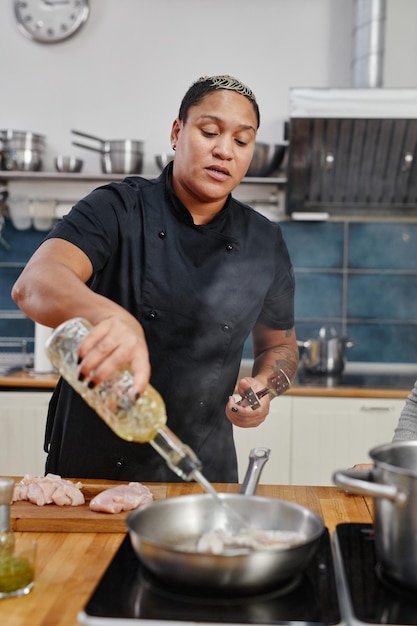 Vertical de la chef femenina tatuada freír la carne mientras se cocina en la cocina profesional