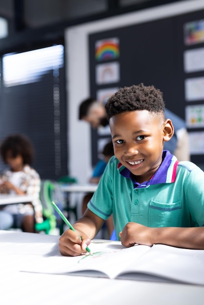 Vertical de um estudante afro-americano feliz em uma mesa em uma sala de aula de escola primária com espaço de cópia