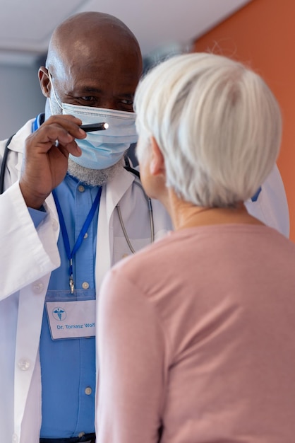 Vertical de diversos médicos de alto rango examinando el ojo de una paciente con linterna, espacio para copiar. Servicios hospitalarios, médicos y sanitarios.