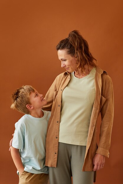 Vertical de feliz madre madura mirando a su hijo mientras está de pie contra la superficie marrón lisa en el estudio