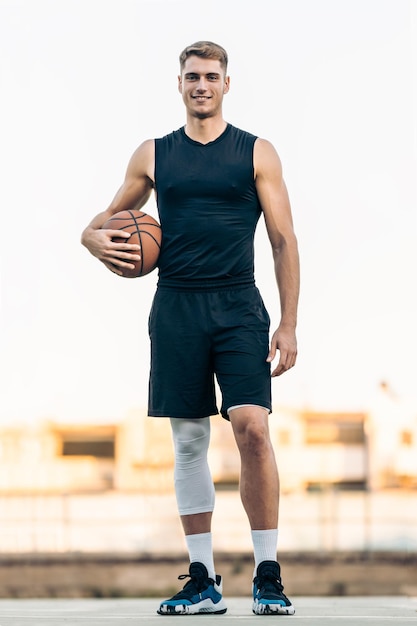 Vertical de un hombre alto de raza caucásica con una pelota de baloncesto de pie al aire libre