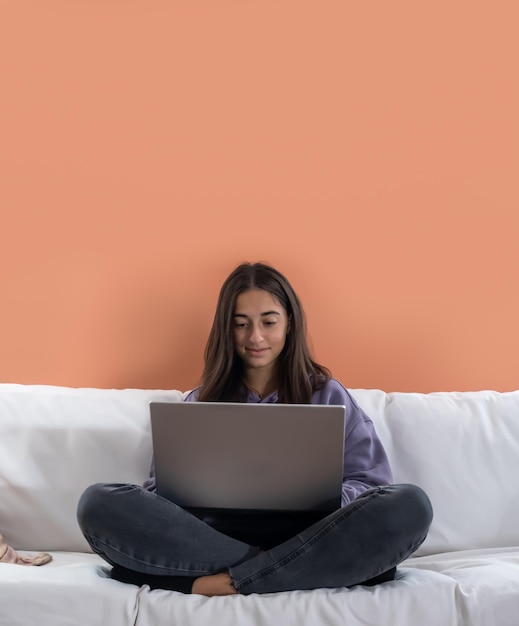 Vertical joven adolescente usando laptop estudiando en casa revisando noticias por correo electrónico en línea en el sofá