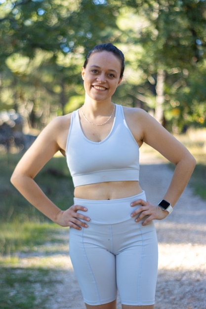 Vertical de una joven mujer deportiva sonriendo a la cámara en la naturaleza con ropa deportiva. concepto de salud y bienestar deportivo