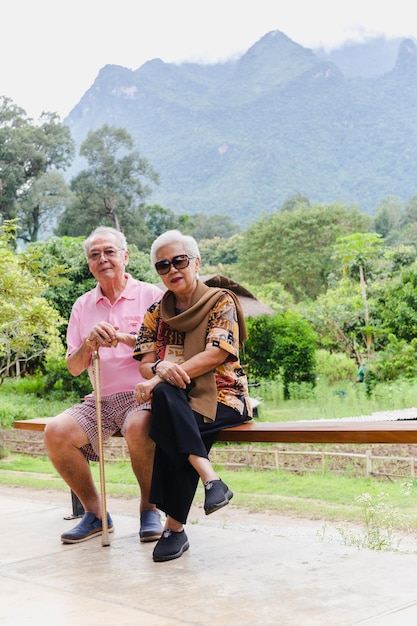 Vertical de pareja senior asiática sentarse en un banco de vacaciones al aire libre