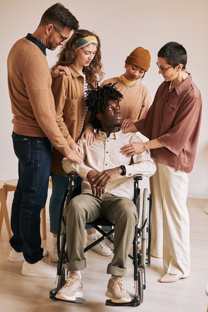 Vertical de personas consolando a joven en silla de ruedas durante la sesión de terapia en el grupo de apoyo