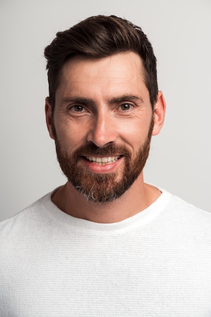 Vertical retrato de feliz guapo barbudo de pie y sonriendo alegre a la cámara. Foto de estudio en interiores, aislado sobre fondo blanco.