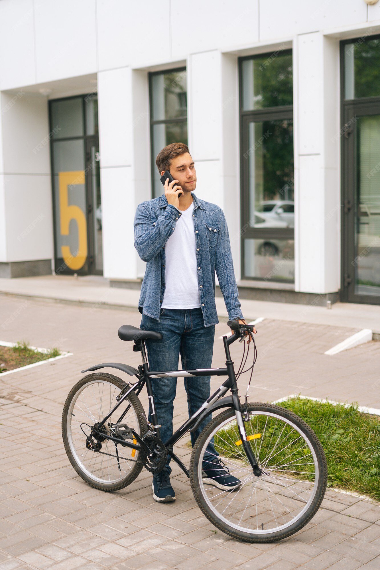 Vertical retrato de joven guapo en casual de pie con bicicleta en las calles de la ciudad y hablando por teléfono móvil. hombre ciclista seguro hablando por teléfono móvil al aire