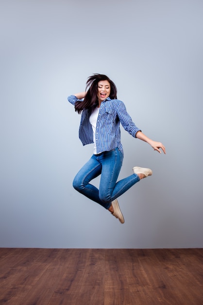 Foto vertical retrato de mujer joven y bonita en camisa a cuadros saltando