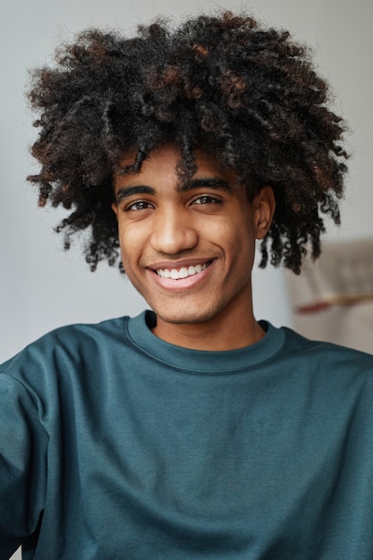 Vertical retrato de sonriente adolescente afroamericano sonriendo a la cámara con enfoque en rizado natural ...