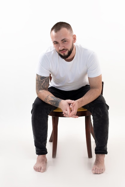 Vertical, sorridente, brutal, homem descalço, sentado no estúdio, olhando para a saúde elegante da câmera