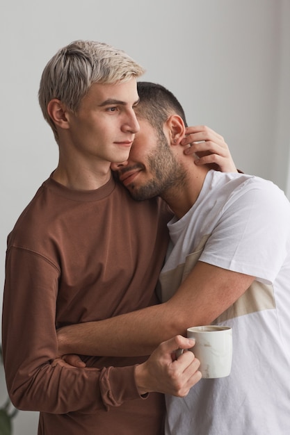 Foto vertical vertical de una pareja gay contemporánea abrazándose tiernamente en interiores en tonos mínimos