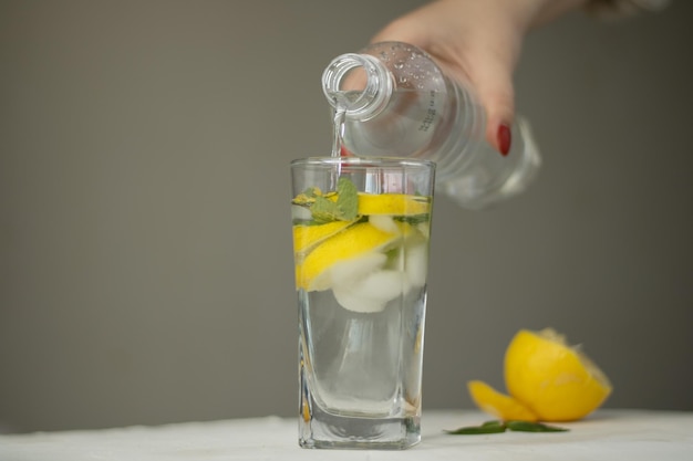 vertiendo agua de botella en vaso en la habitación. una mano femenina vierte agua de una botella