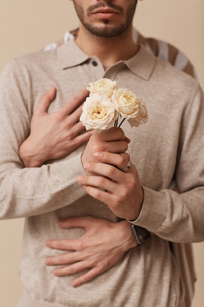 Vertikal abgeschnittene Aufnahme eines nicht erkennbaren schwulen Paares, das Blumen im Studio umarmt und hält