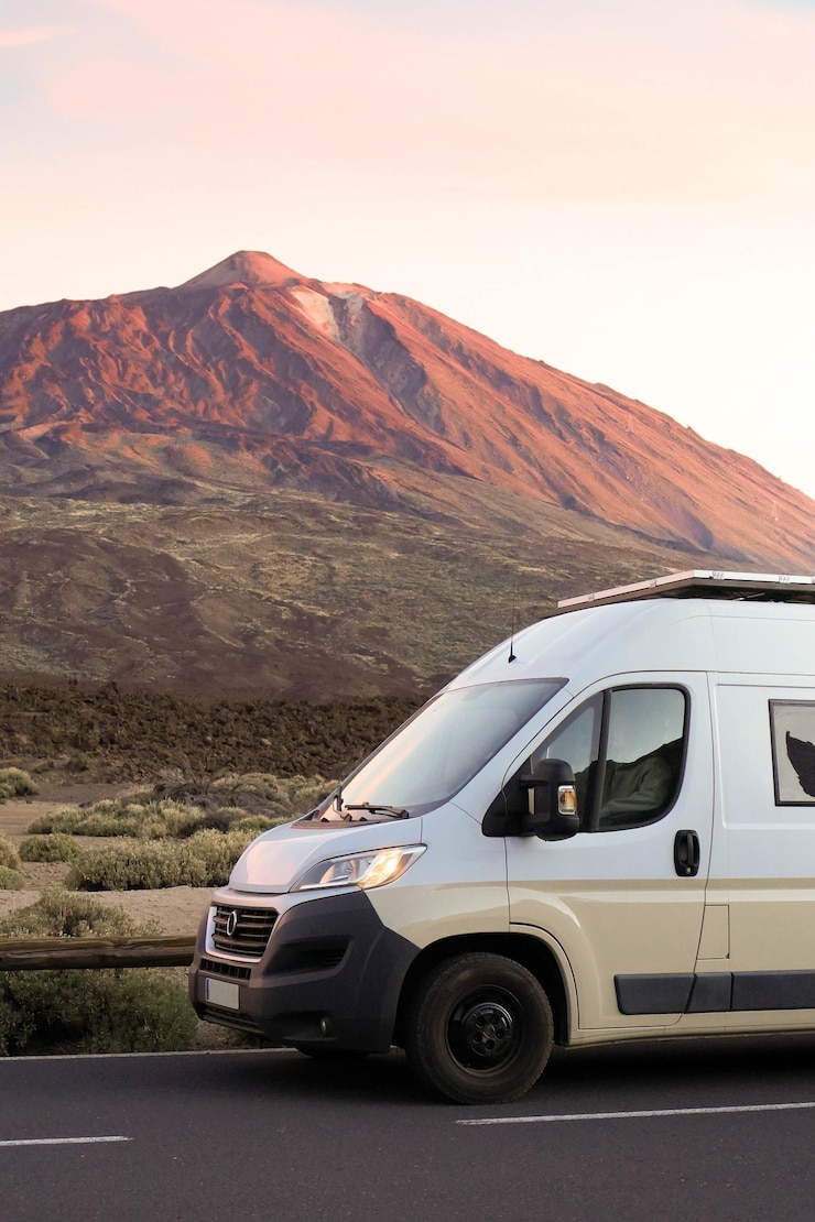 Foto vertikalansicht des sonnenuntergangsglühens auf einem lieferwagen, der in der nähe eines berges auf der teide auf teneriffa fährt
