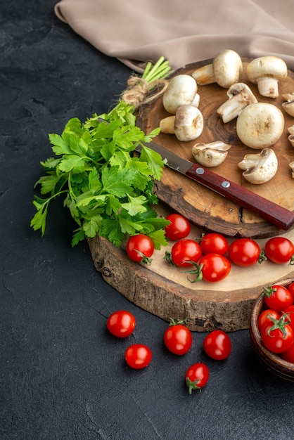 Vertikale Ansicht von frischen rohen Pilzen und grünen Bündelmessertomaten auf Holzbretttuch auf schwarzem Hintergrund