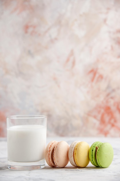 Vertikale Ansicht von frischer Milch in einer Glastasse neben bunten leckeren Macarons auf pastellfarbener Oberfläche