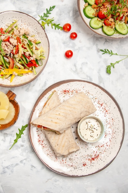 Vertikale Ansicht von gesunden veganen Salaten getrockneten Ananas und Lavash Wraps auf befleckter weißer Oberfläche