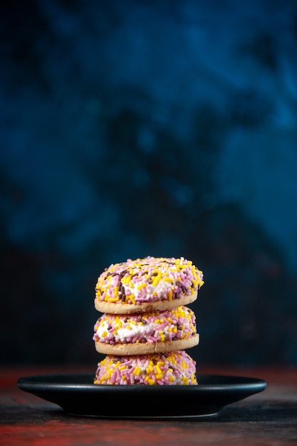 Vertikale Ansicht von hausgemachten leckeren Zuckerkeksen auf schwarzem Teller auf dunklem Hintergrund mit Mischfarben