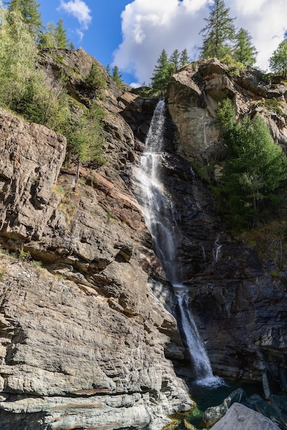 Vertikale Aufnahme des Lillaz-Wasserfalls, der über Granitfelsen mit spärlicher Vegetation fließt Aostatal