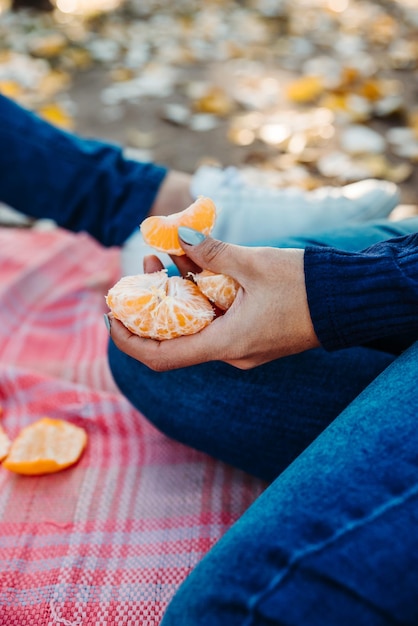 Vertikale Aufnahme einer Frau, die auf einer Picknickdecke in einem Park sitzt und geschälte Mandarinen hält