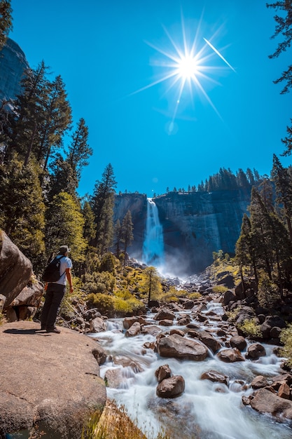 Vertikale Aufnahme einer Frau vor dem Wasserfall und den Bäumen im Yosemite-Nationalpark