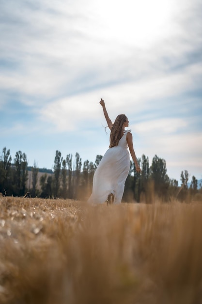 Vertikale Aufnahme einer fröhlichen Frau in einem weißen Kleid, die im Sonnenlicht durch ein Feld läuft
