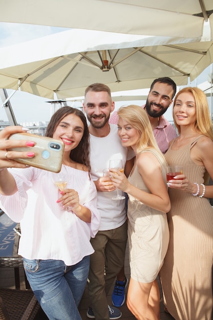 Vertikale Aufnahme einer Gruppe junger Leute, die Sommer auf Dachparty feiern, Selfies mit Smartphone nehmend