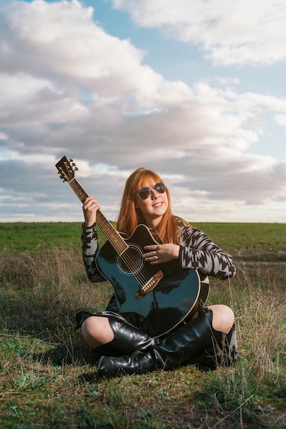 Foto vertikale aufnahme einer kaukasischen sängerin und songschreiberin mit einer gitarre, die im gras des feldes sitzt