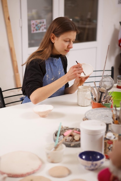 Vertikale Aufnahme einer Künstlerin, die Keramikschale im Töpferstudio dekoriert