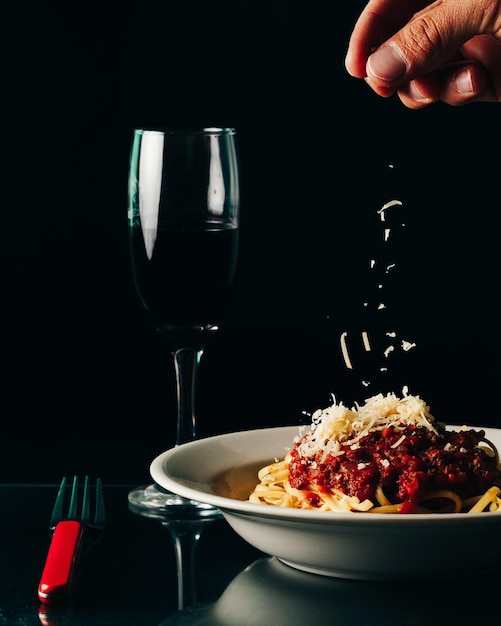 Vertikale Aufnahme einer Person, die Parmesan auf Nudeln mit Soße mit einem Glas Wein auf den Tisch legt