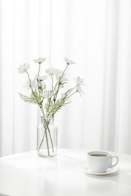 Vertikale Aufnahme einer Tasse Kaffee neben einer Vase voller schöner weißer Blumen im Innenbereich