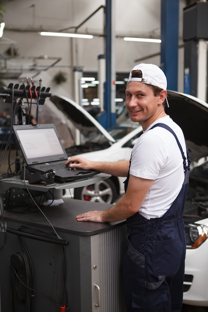 Vertikale Aufnahme eines fröhlichen Automechanikers, der einen Computer in der Garage verwendet und ein Auto repariert