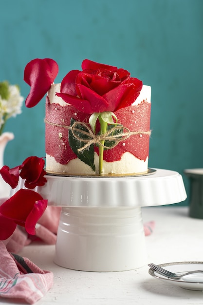 Vertikale Aufnahme eines kleinen Kuchens mit einer roten Rose auf einem weißen Tablett